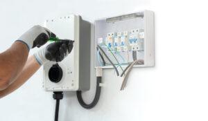 A man electrician installing a home charging, installing charging station for electric car at private house