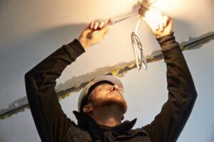 portrait-of-male-electrician-focused-on-wiring-a-temporary-light-bulb-fixtur