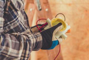 A technician holds a multimeter while wearing gloves, examining electrical readings on a construction site in bright daylight.