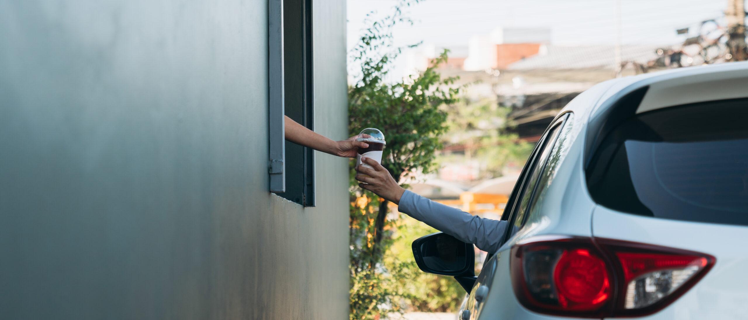 Young man receiving coffee from drive-thru counter, convenient takeaway service for safety and protection.